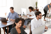 In einem Büro arbeitet eine Gruppe von Fachleuten an Laptops und PCs.